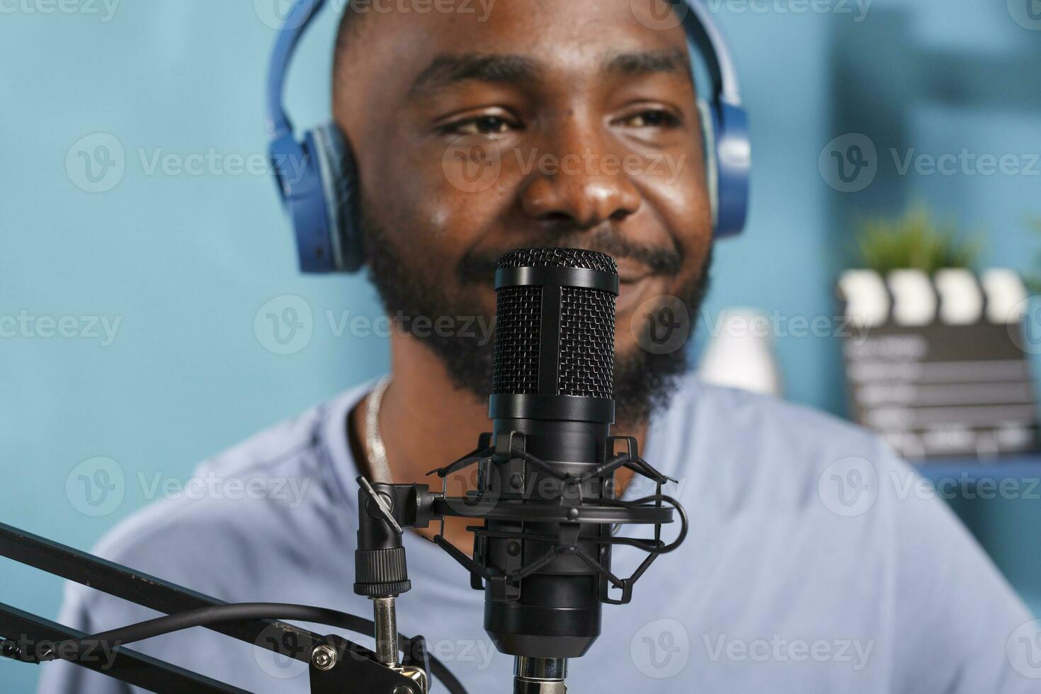 African american man in headphones speaking in microphone while broadcasting podcast. Young blogger wearing headset talking in mic while recording digital video content close up photo