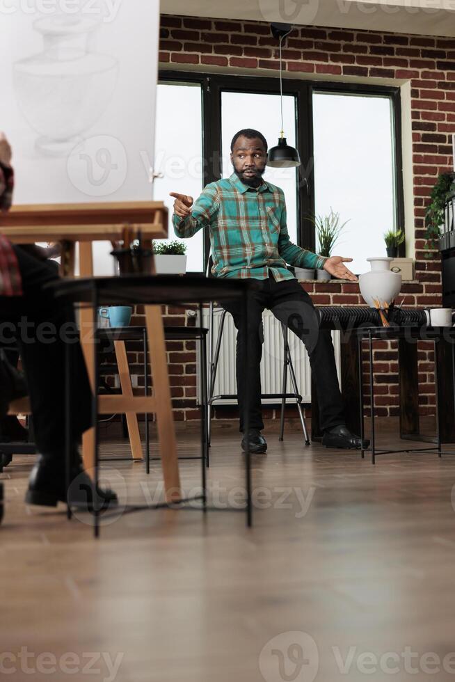 Young African American man art teacher talking with students during group drawing class, encouraging creativity and selfexpression. Creative inspired black guy teaching artist workshop photo