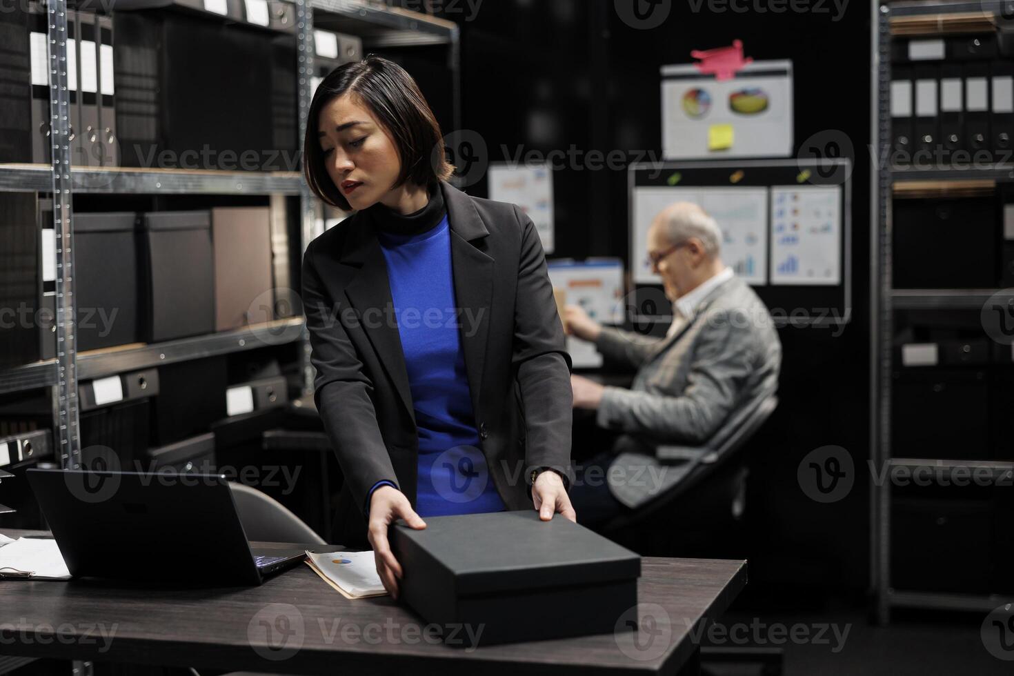 Professional asian accountant checking bureaucratic analytical data paperwork in file cabinet room office surrounded by accountancy statistic reports. Businesswoman in storage repository photo