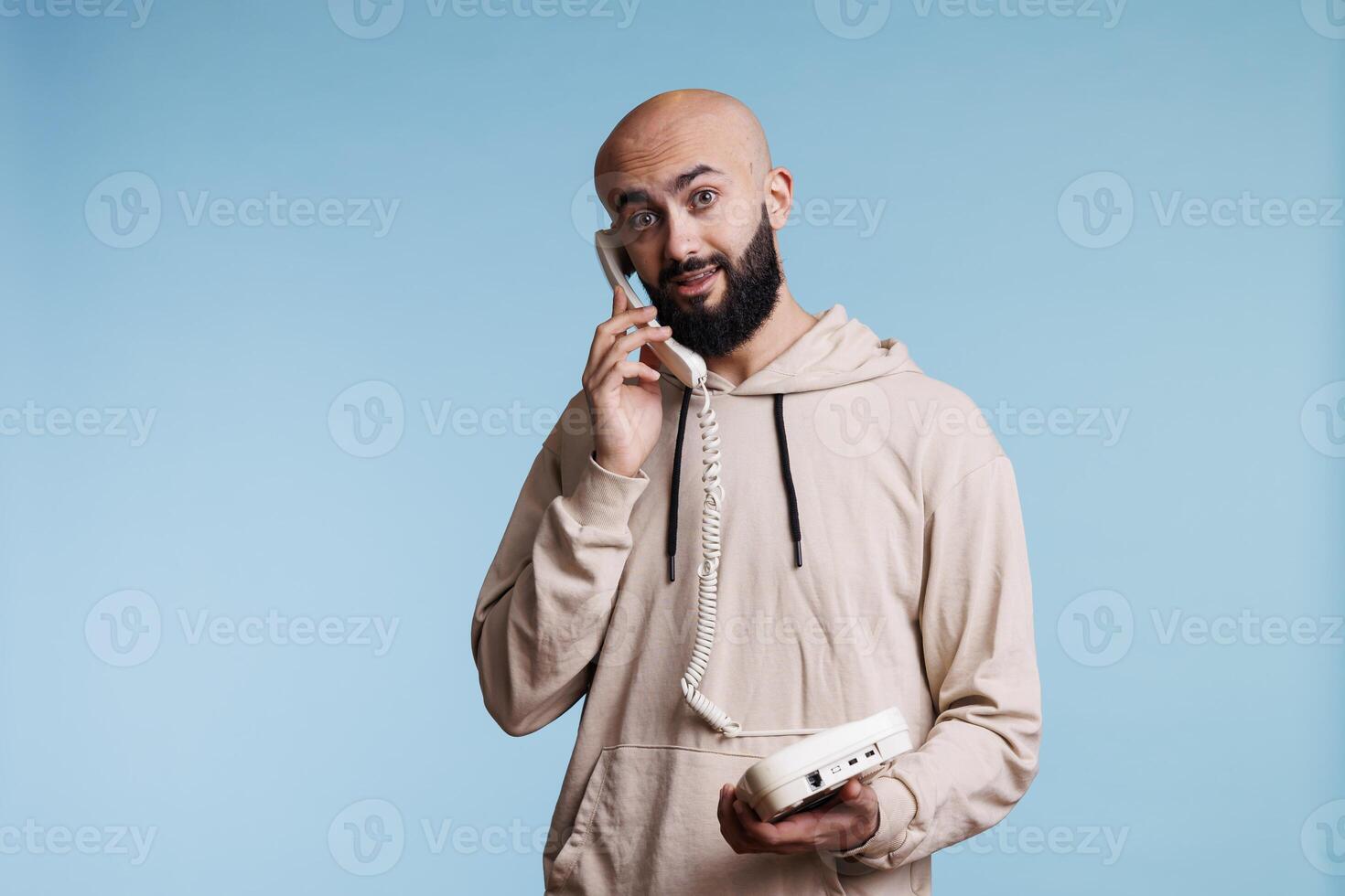 Excited arab man answering call while holding old fashioned landline phone portrait. Young person having conversation on retro telephone and looking at camera with amazed expression photo
