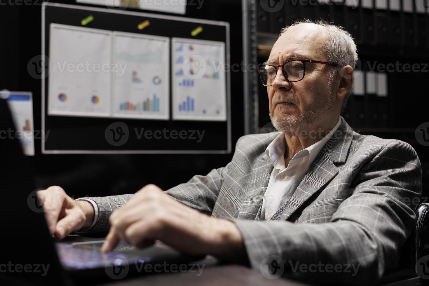 Accountant employee checking administrative analytical statistics in dark cabinet room office. Professional businessman in file storage room surrounded by accountancy reports photo