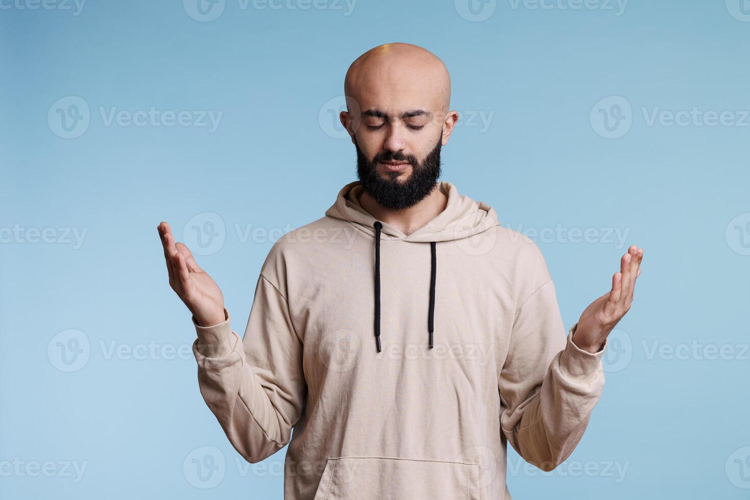 Arab man praying to god with open hands and closed eyes, pleading for blessing and forgiveness. Young spiritual person praising and pleading for peace with raised arms gesture photo