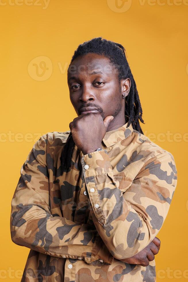Pensive man brainstorming ideas in studio over yellow background, feeling confused and wondering about idea and question. African american person showing contemplative expression photo