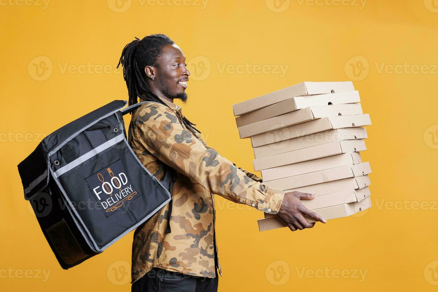 Pizzeria courier holding stack full of pizza boxes, preparing delivery for clients during lunch time. African american worker with takeout thermal backpack delivering takeaway food order photo