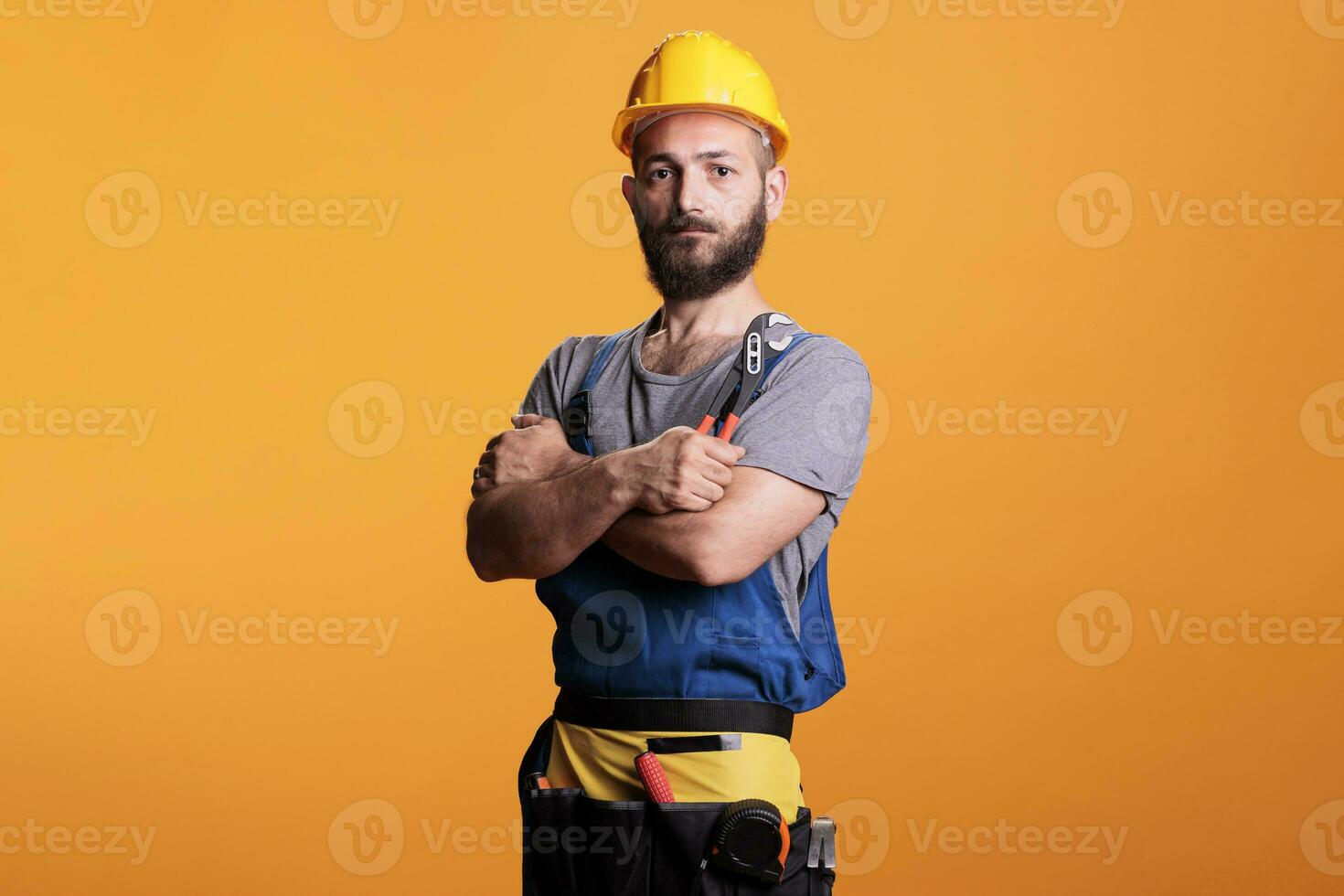 Confident male contractor holding pair of pliers to work on house renovation, standing in studio. Construction worker foreman using pliers and refurbishment tools, industrial engineering. photo