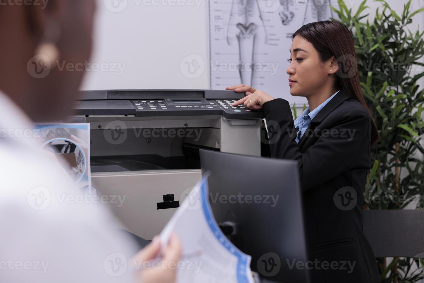Asian reception worker scanning medical documents while doctor discussing patient expertise with assistant, standing at hospital counter. Staff planning health care treatment in waiting room photo