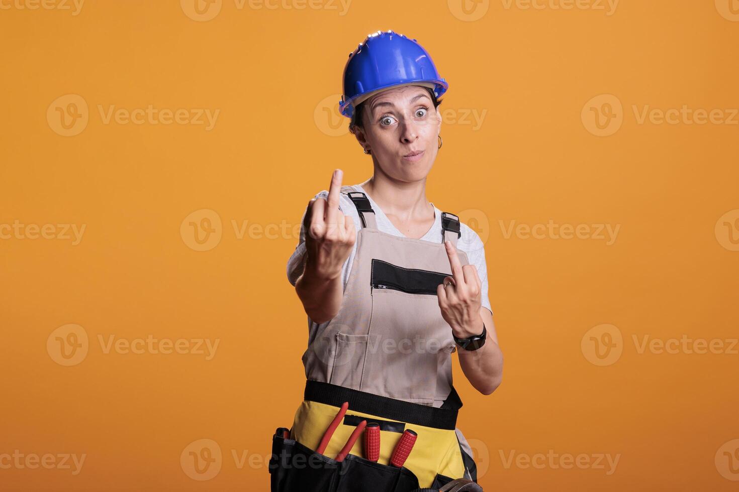 Angry female builder showing middle finger in studio, doing rude gesture and acting aggressive. Making disapproving signs and expressing negative emotion, displeased handywoman. photo