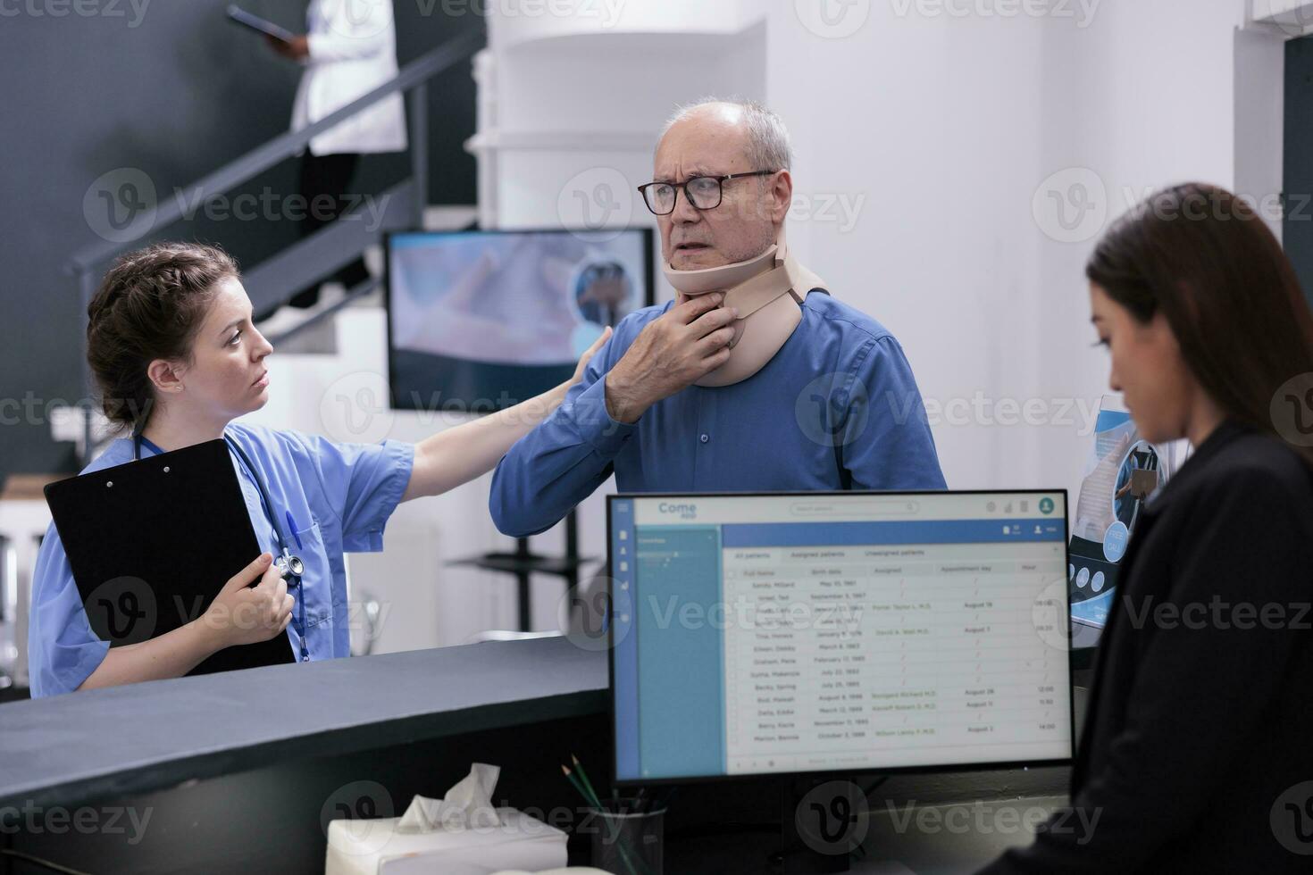 Senior patient with cervical neck collar explaining symptoms to medical nurse discussing health care treatment, standing at hospital counter. Injured man waiting to attend checkup visit appointment photo