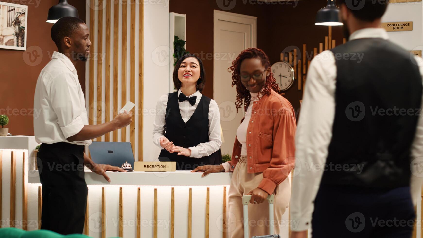 Weary hotel guests ready to be checked in their room after long flight, receiving access key card from asian receptionist. Tourists being assisted with their luggage by professional bellboy photo