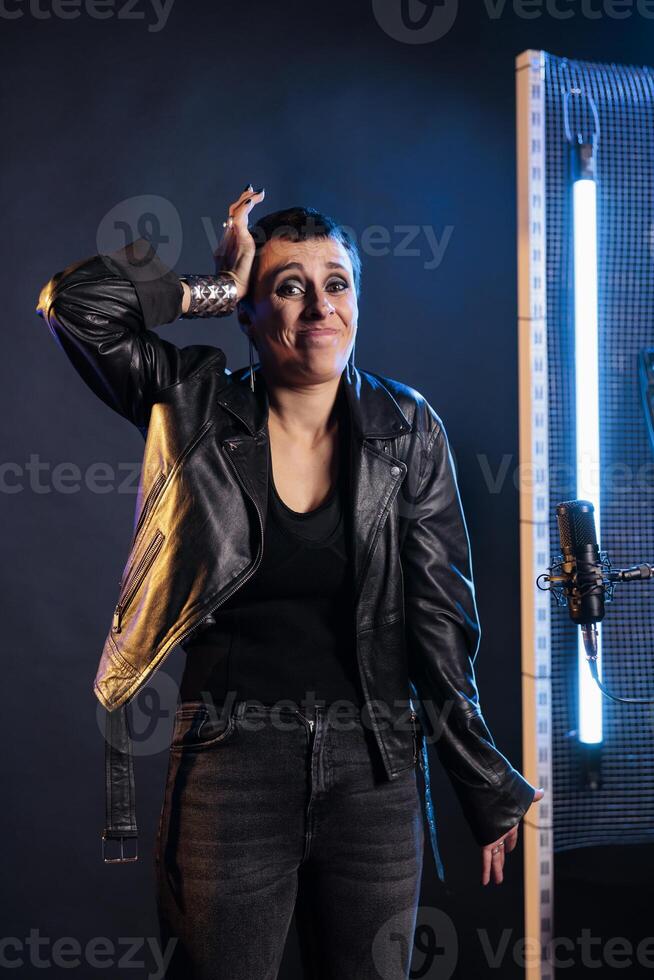 Confused musician having uncertain expression standing in front of microphone preparing to sing heavy metal song, working at rock album. Artist playing grunge music using electric guitar instrument photo