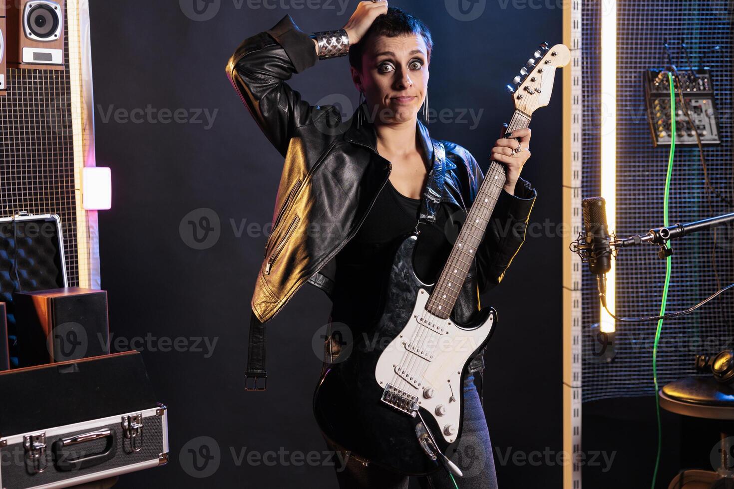 Confused rock musician having uncertain expression while standing in sound studio working at grunge album, preparing heavy metal song using electric guitar. Dont know gesture concept photo