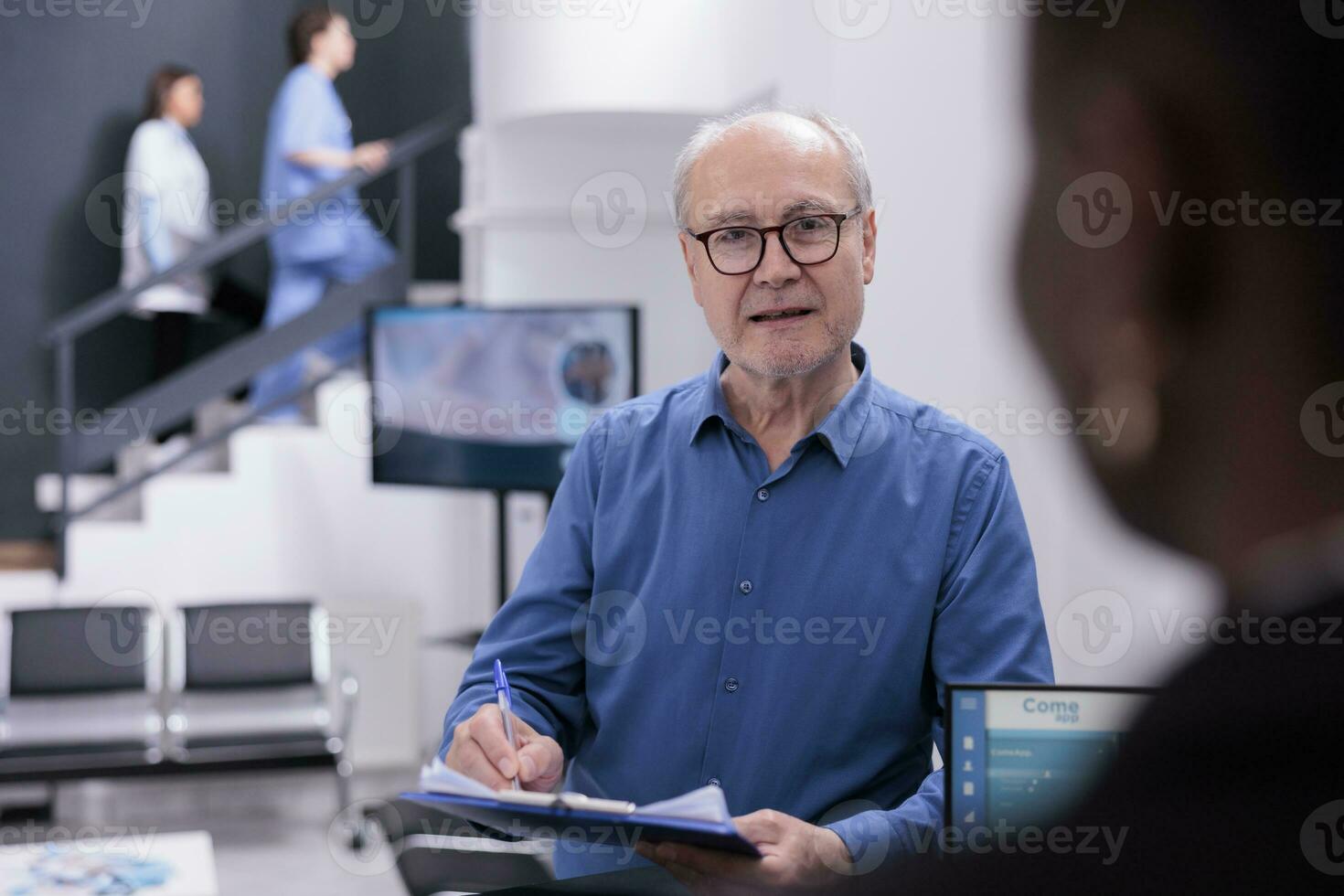 Caucasian man standing at reception counter asking receptionist for help with medical documents, discussing about insurance before start examination with medic. Health care concept photo