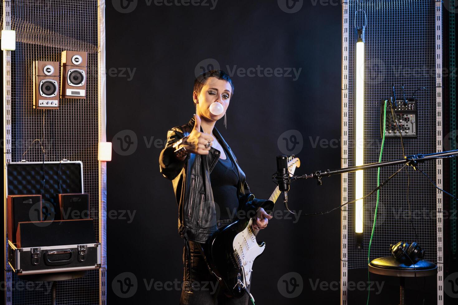 Woman guitarist showing approval sign at camera while performing metal music in sound studio using electric guitar. Rebel performer doing thumbs up gesture, playing rock song at solo performance photo