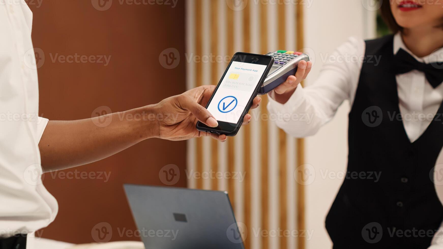 Close up of african american tourist using smartphone banking app to pay for room upgrade during check in process. Receptionist using POS payment terminal to validate credit card purchase photo