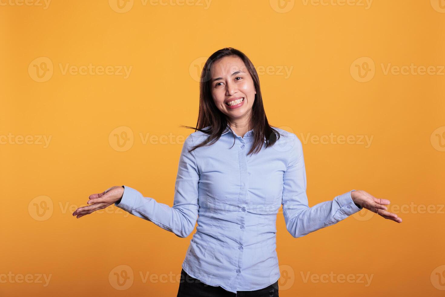Doubtful filipino woman being hesitant and unconfident while trying to answering question. Confused and clueless model shrugging shoulders having uncertain expression in studio over yellow background photo