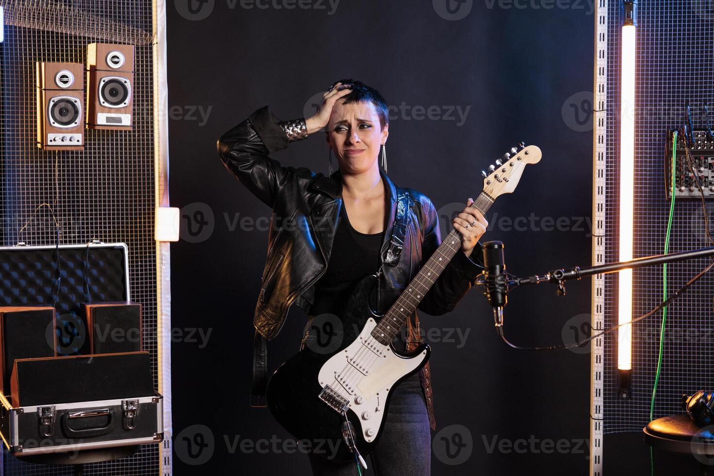Upset rockstar forget the rock song while playing at electric guitar preparing for grunge concert in sound studio, working at new album. Superstar woman in leather outfit using electricinstrument photo
