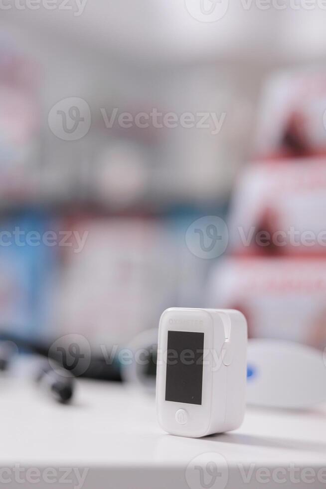 Medical oximeter standing on table in empty pharmacy ready to be used by customer, digital device to measure oxygen saturation. Drugstore filled with drugs, vitamins and pharmaceutical products photo