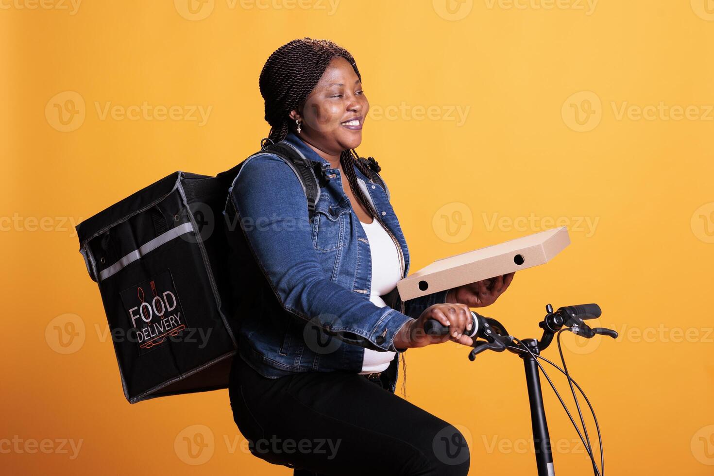 Takeout deliverywoman carrying pizza cardboard delivering takeaway order to customer during lunch time, using bicycle as transportation in studio. Take out food service and concept photo