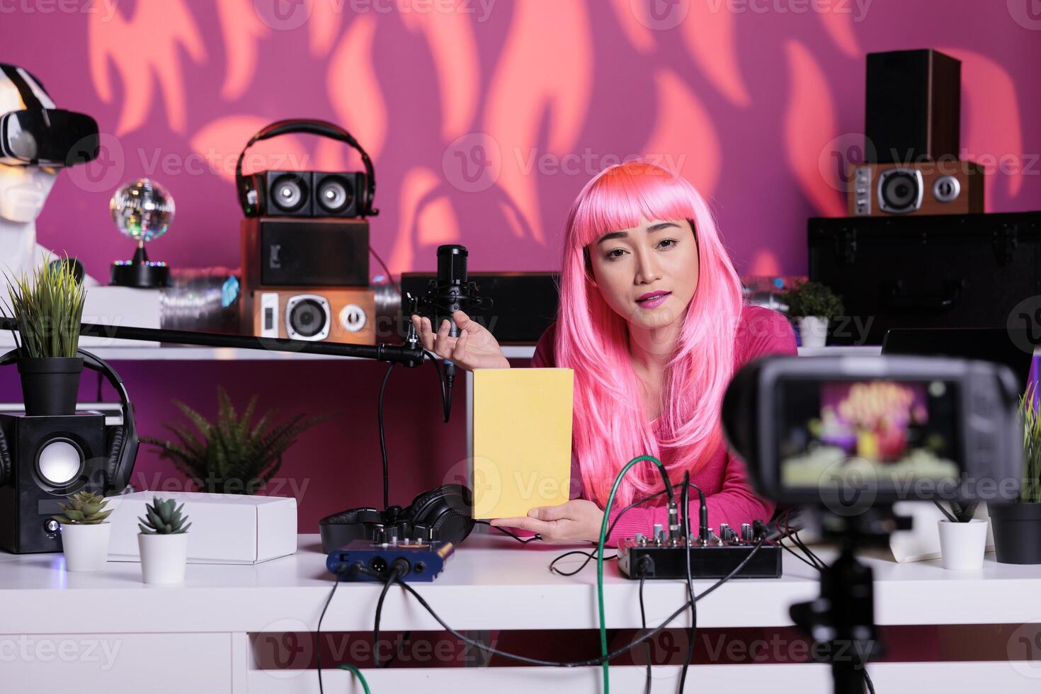 Influencer with pink hair and tshirt presenting notebook recommendation reviewing school product in front of camera while filming vlog. Content creator using professional broadcast equipment photo