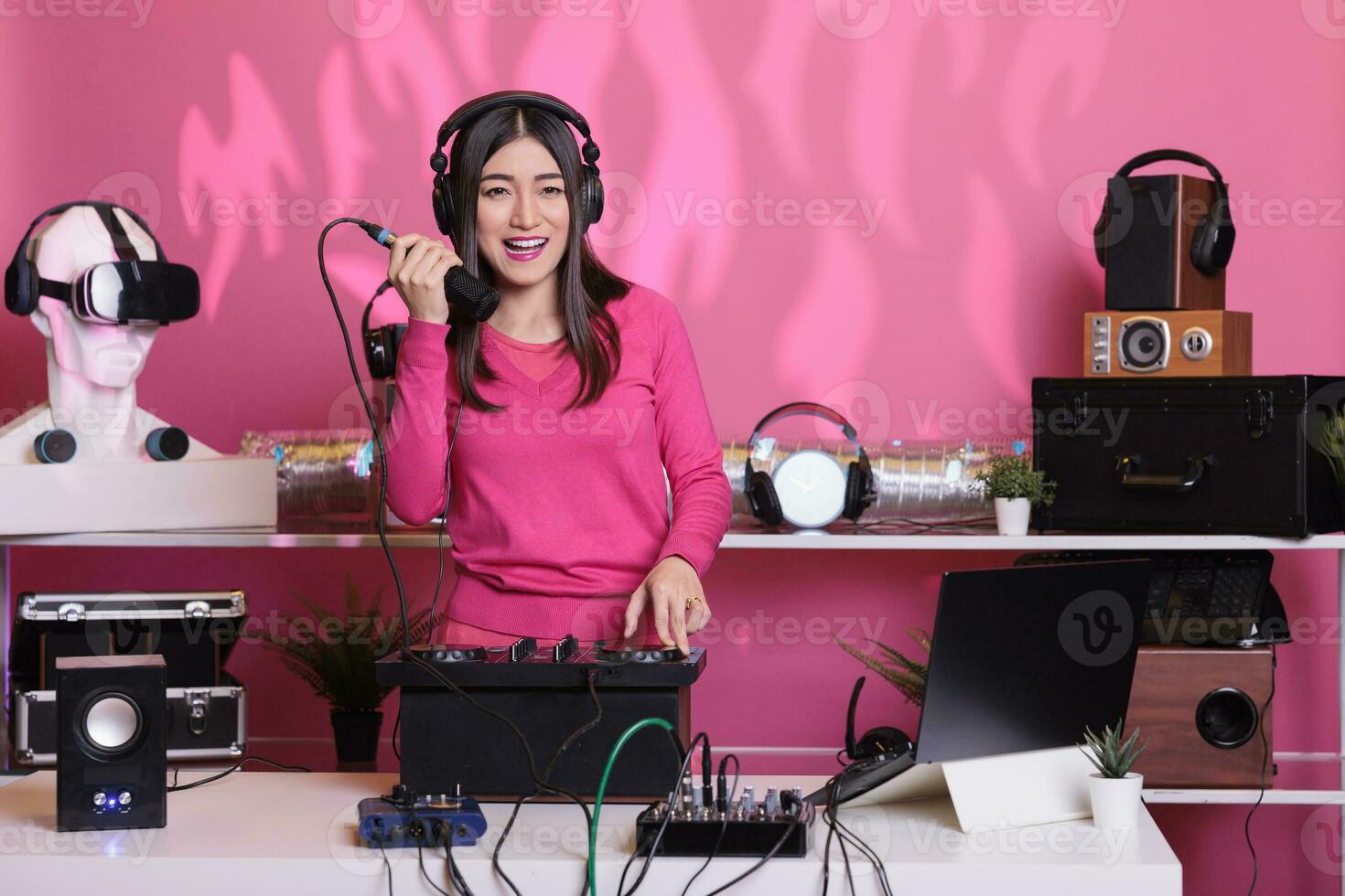 Smiling musician talking into microphone with fans while mixing electronic sounds with techno, enjoying to party at night. Asian artist creating musical performance with remix music photo