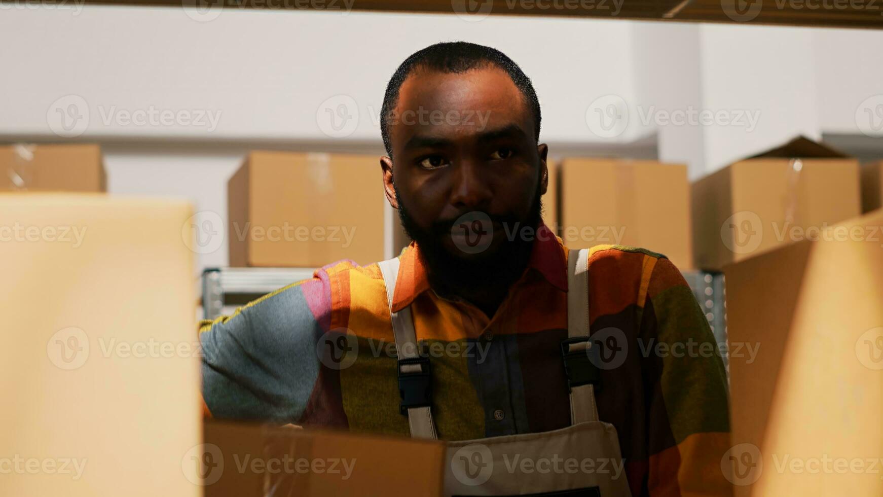 Young man organizing boxes in depot, moving cargo in cardboard packs for retail store delivery. Warehouse employee carrying packages on shelves, doing inspection. Handheld shot. Close up. photo