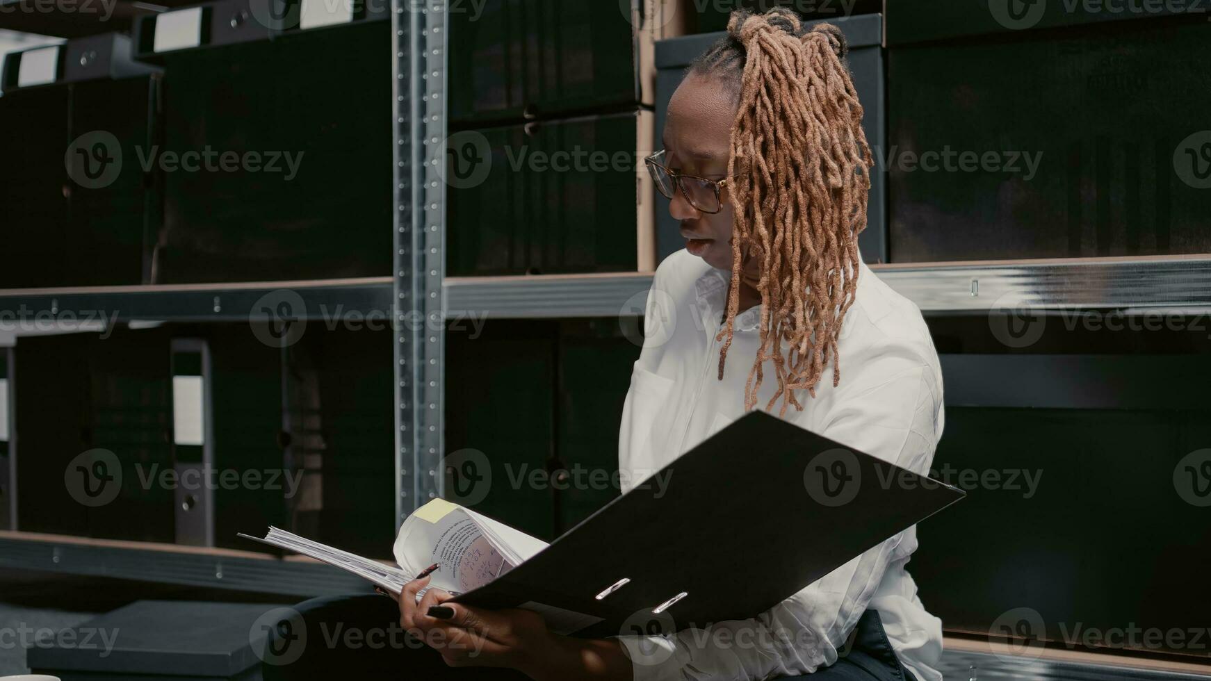 Law agent reading case files in police archive room, working on criminal investigation. Private investigator using physical evidence and surveillance photos to do research. Tripod shot.