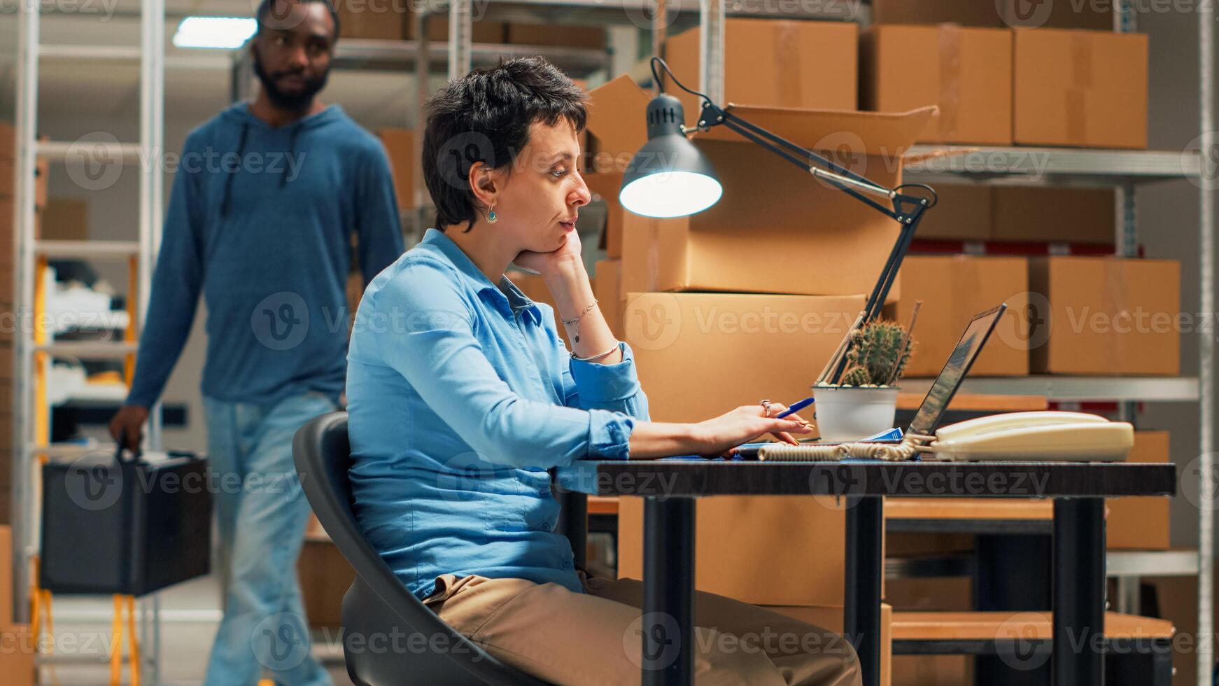 Man and woman checking inventory and stock before shipping merchandise order, working on business plan at storehouse. Owner typing data on laptop, doing quality control. Handheld shot. photo