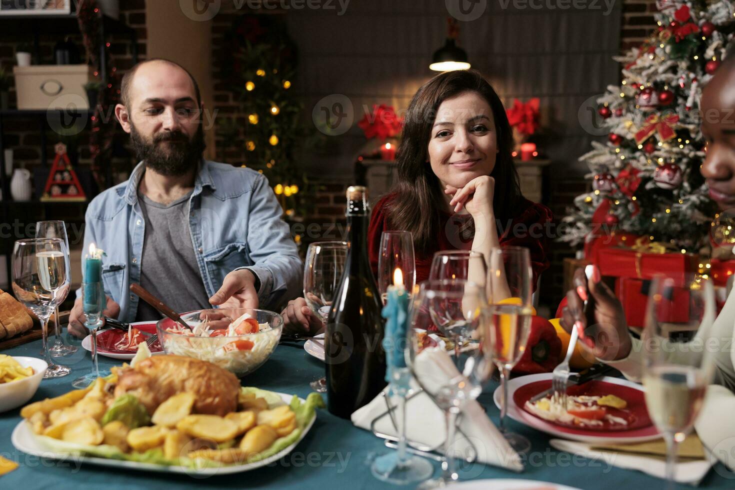 joven Pareja celebrando Navidad con familia, mujer asistiendo festivo cena durante Navidad víspera fiesta a hogar. personas disfrutando tradicional comida en el mesa, sensación alegre y alegre. foto