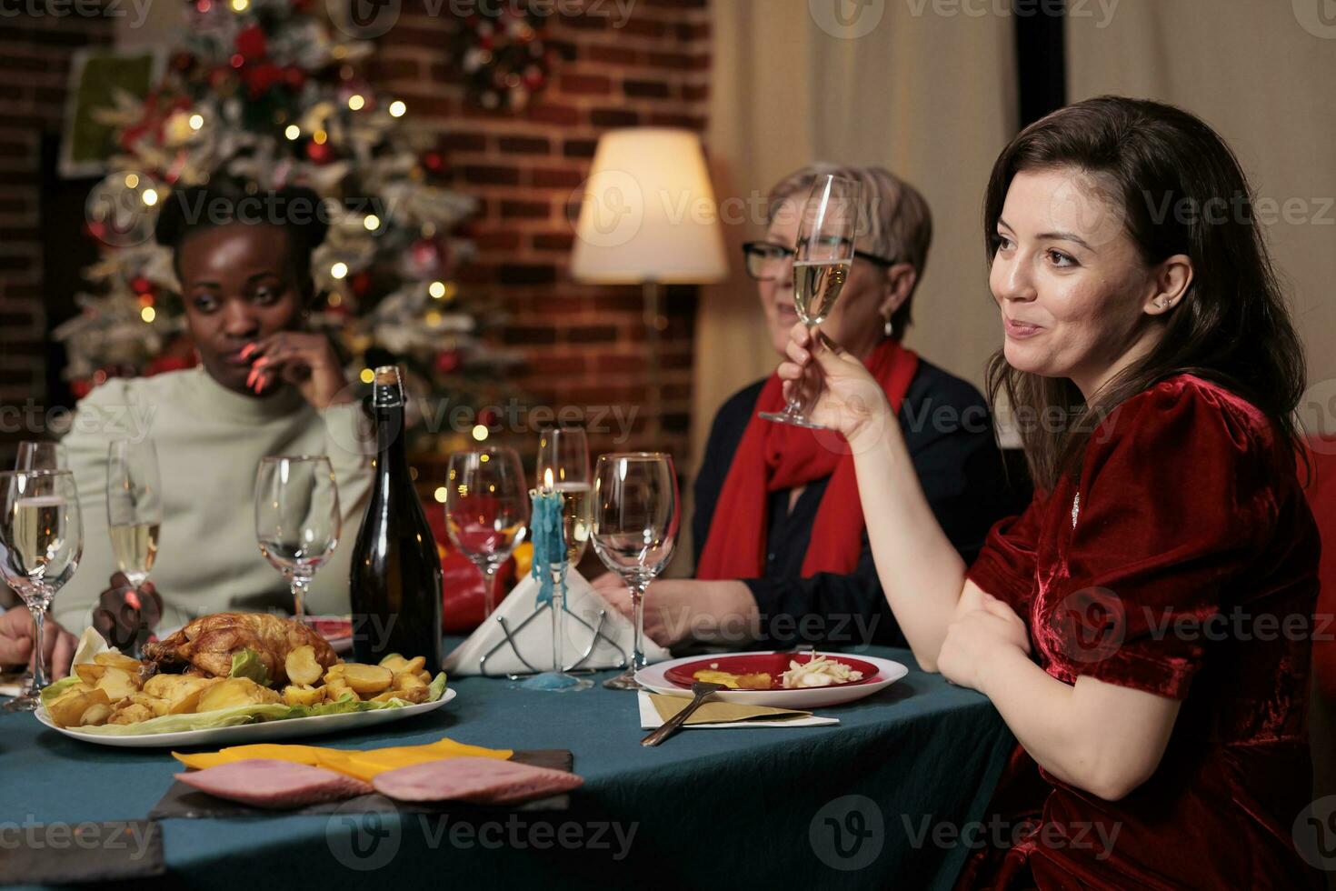 Persons raising glasses for cheers during christmas eve dinner, enjoying family time at home with homemade meal. Diverse people making toast to thank friends for celebrating around the table. photo