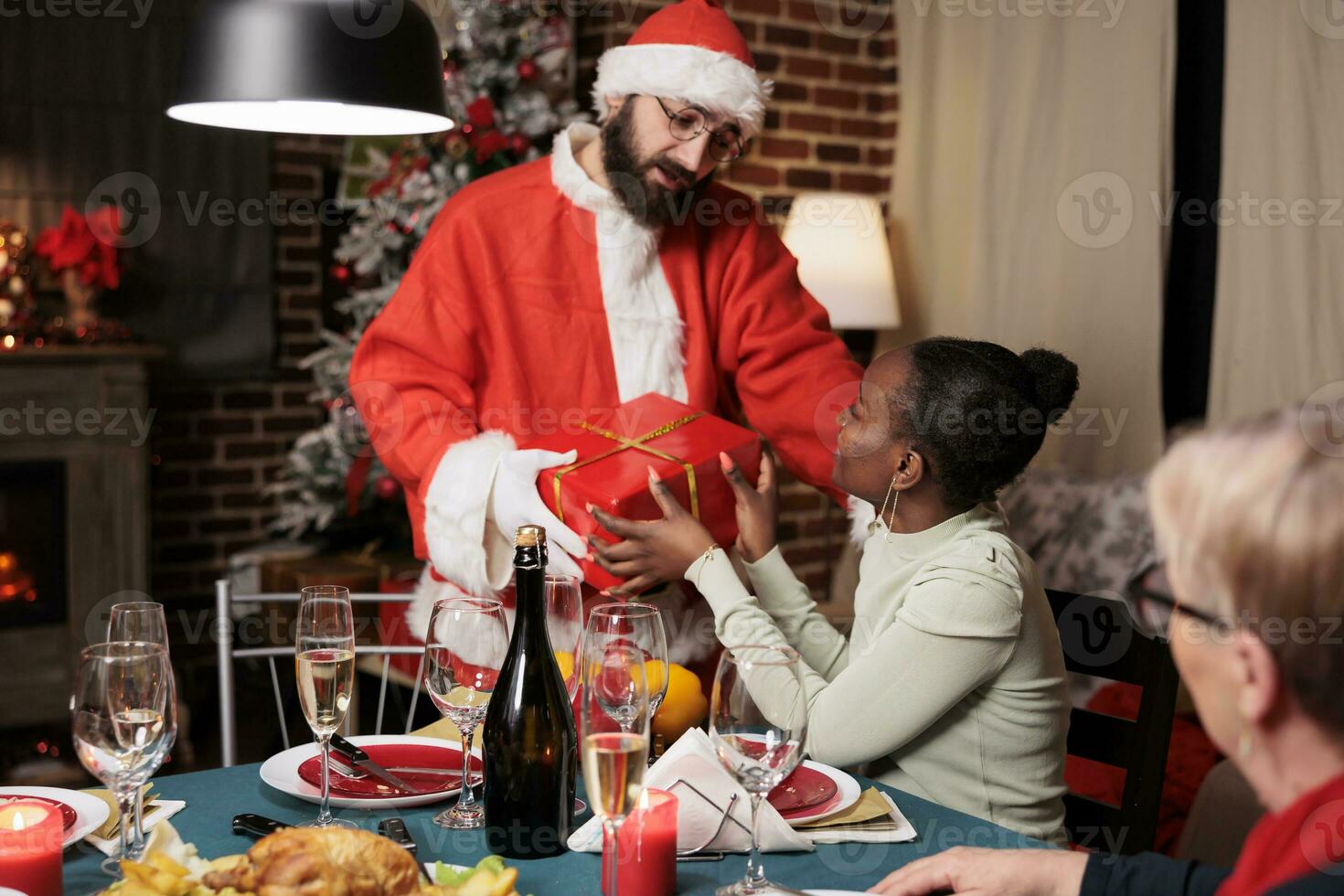 Santa claus handing gifts to people at festive dinner, spreading christmas spirit and enjoying december festivity. Person dressed in costume and hat offering presents to friends and family. photo