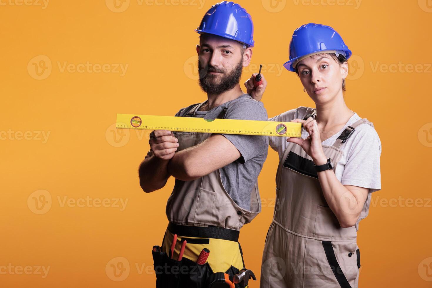 Construction workers holding screwdriver and water level in studio shot, using ruler or leveler to work on renovation. Team of building experts being confident with renovating tools. photo
