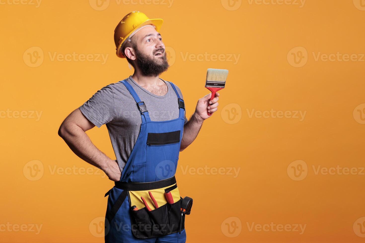 Young painter decorator painting walls with brush in studio, posing with paintbrush and tools before working on renovation. Craftsman expert using brush and color to do diy project. photo