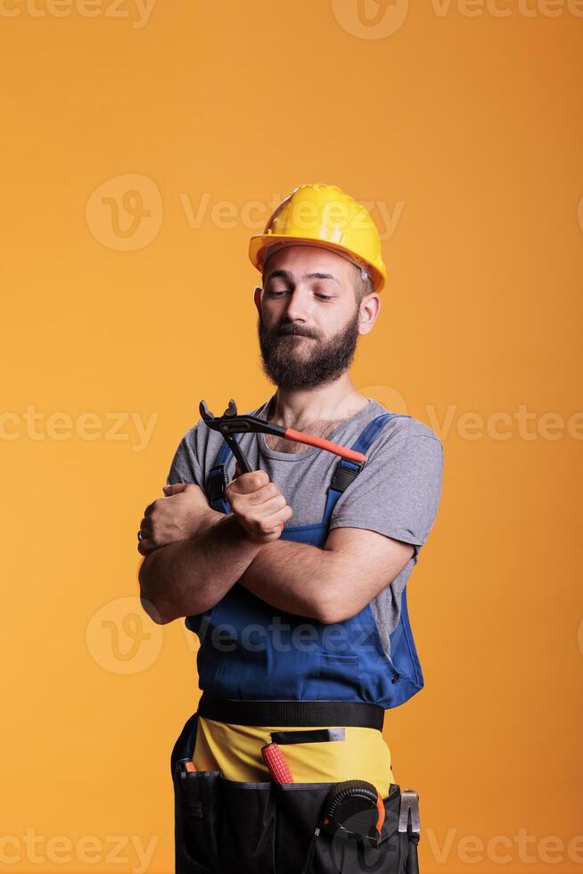 Professional repairman holding pair of pliers to work on house renovation, standing in studio. Construction worker foreman using pliers and refurbishment tools, industrial engineering. photo