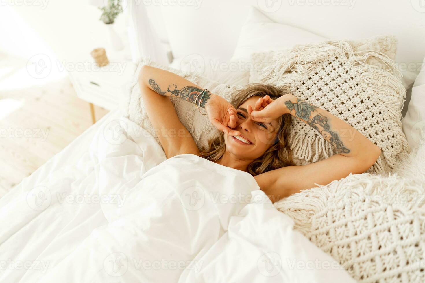 Laughing woman chilling in her bed. Tatoo on hends. Cozy home lifestyle. photo