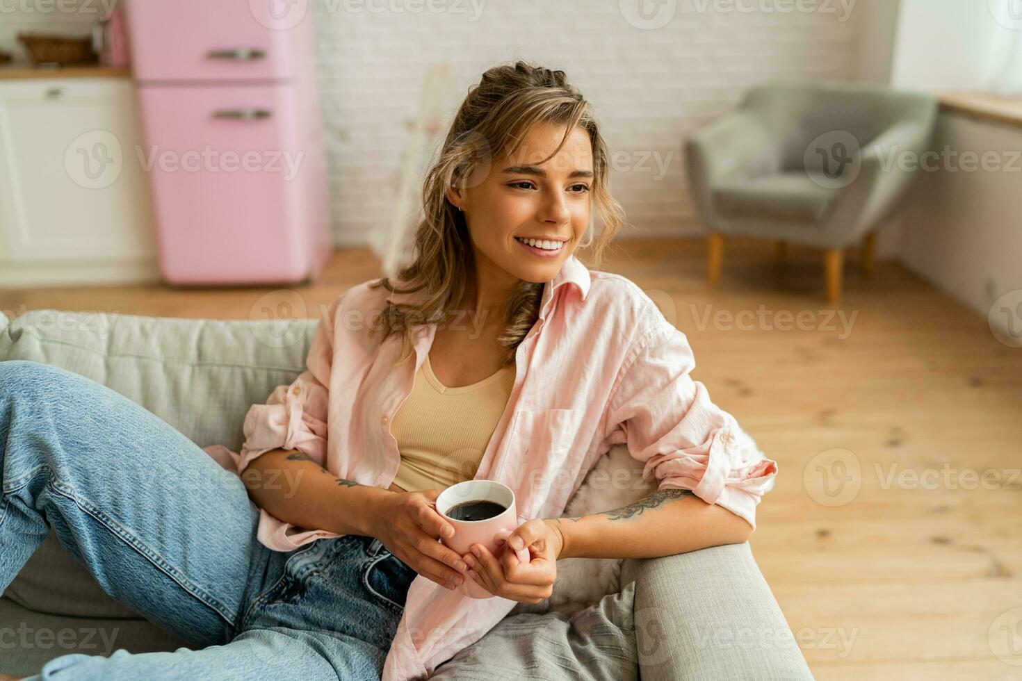 Graceful woman in casual clothes resting un sofa in cozy  living room. Holding cup of  tea. photo