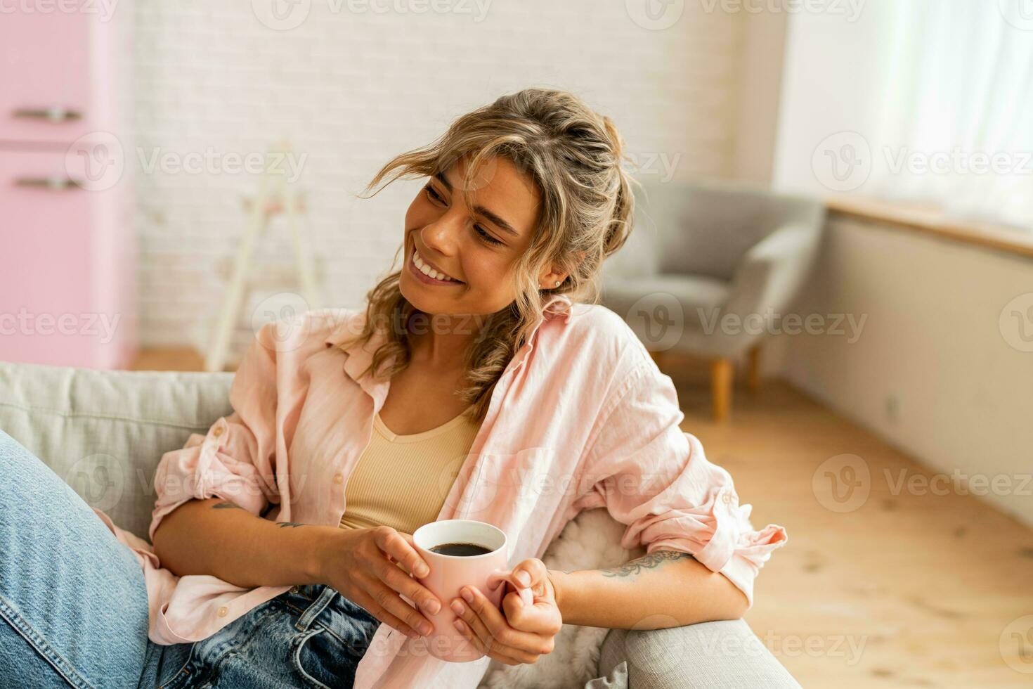 Graceful woman in casual clothes resting un sofa in cozy  living room. Holding cup of  tea. photo