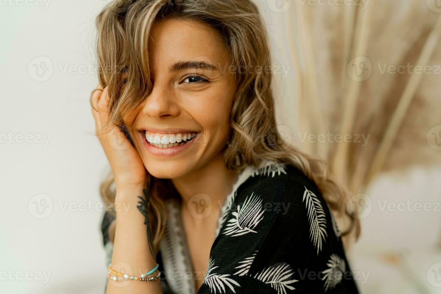 Close up portrait of  blond woman with perfect smile in stylish boho autfit. Posing in inerior studio over white background. photo