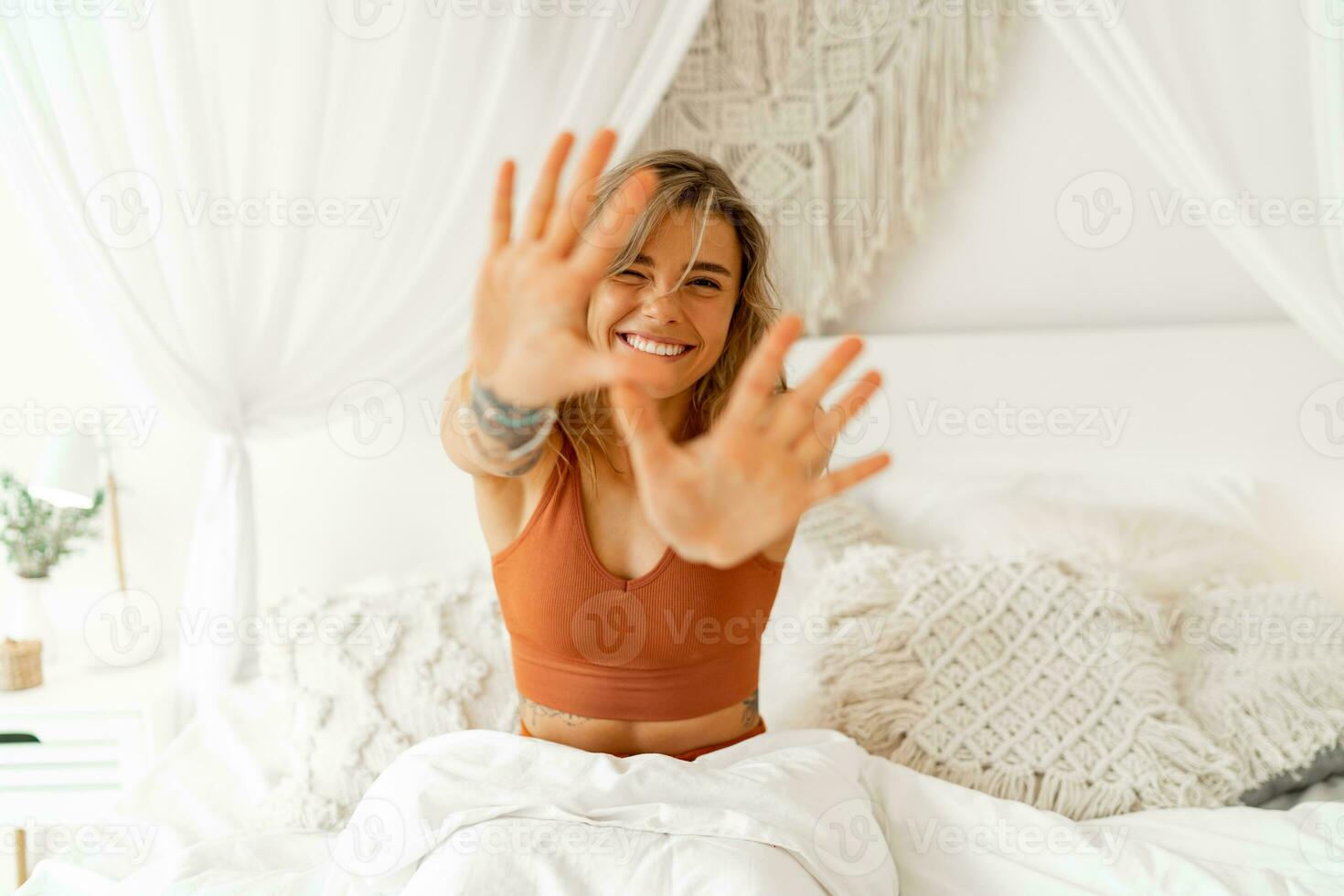 Smiling  young woman stretching in bed waking up in cozy bedroom with bohemian interior style. Female wearing in comfort pajamas enjoying early morning,. photo