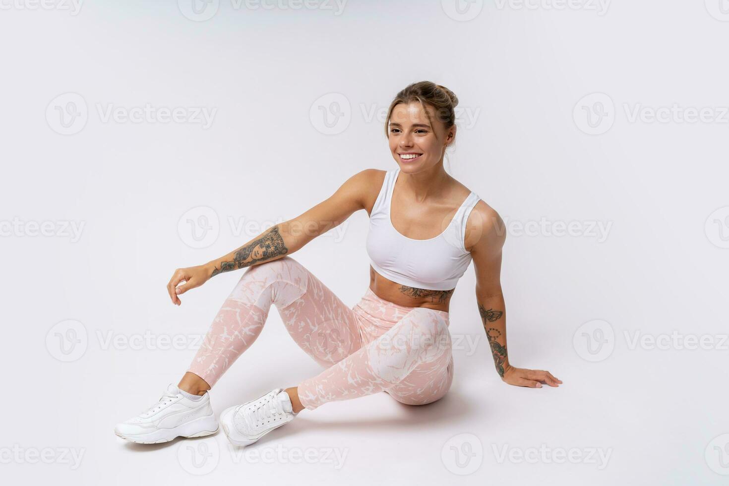 Fitness and lealthy lifestyle concept. Happy sporty young woman sitting on the floor at studio after exercising, resting and looking at camera. White background. photo