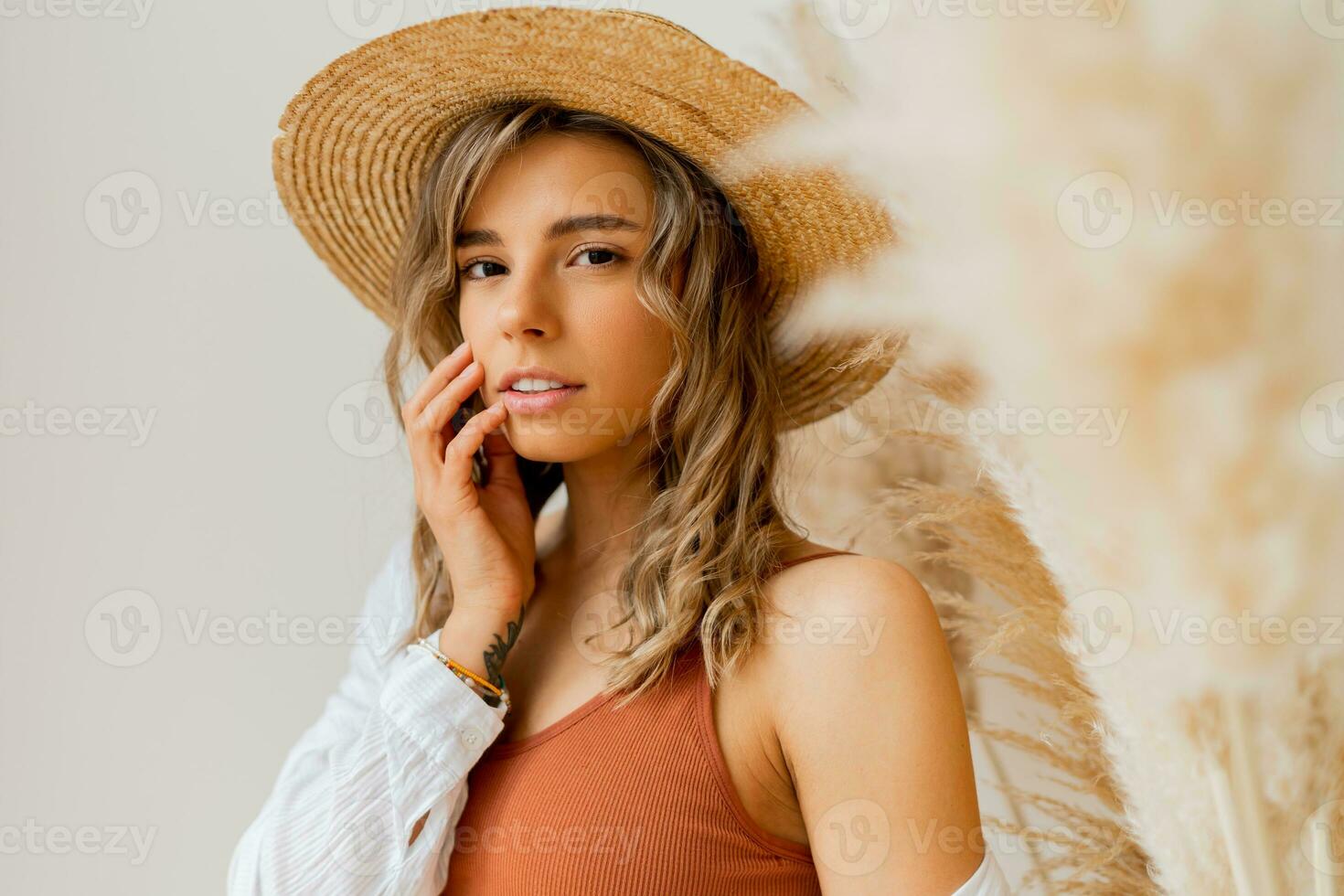 cerca arriba retrato de atractivo mujer en verano atuendo con Paja sombrero posando terminado blanco antecedentes en estudio con pampa césped decoración. foto