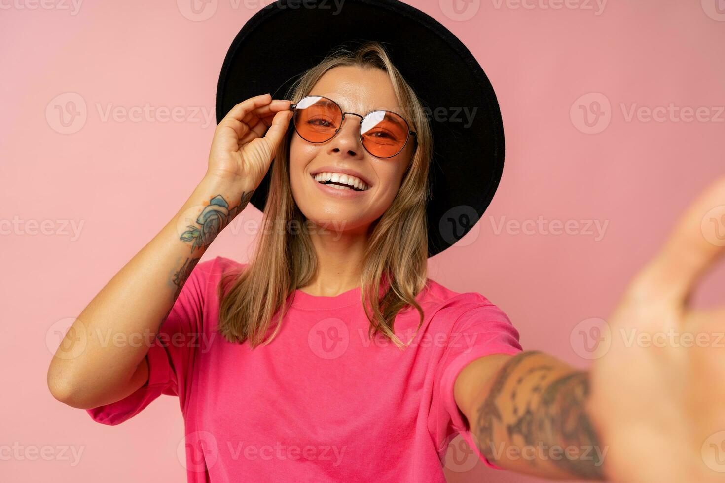 cerca arriba estudio foto de sonriente joven mujer con tatuaje en manos posando terminado rosado antecedentes.