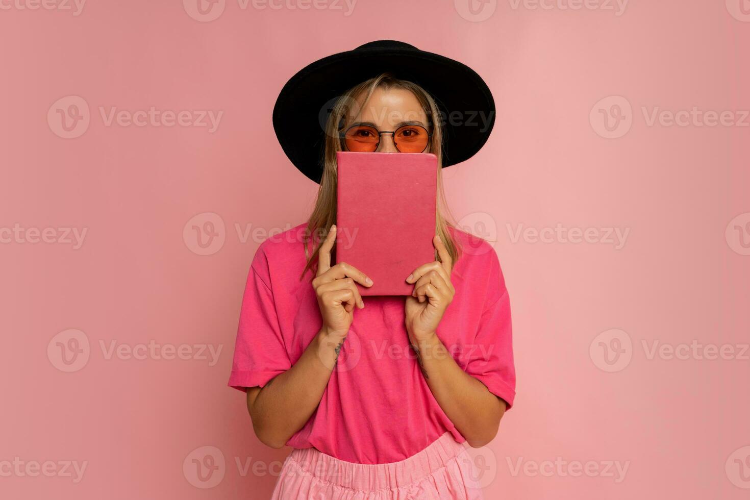 linda rubio mujer en negro sombrero y rosado primavera atuendo participación libro y posando en estudio. foto