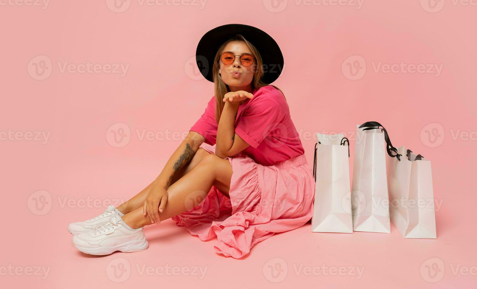 Pretty smiling woman in  spring trendy outfit posing with white shopping bags in studio over pink background. photo