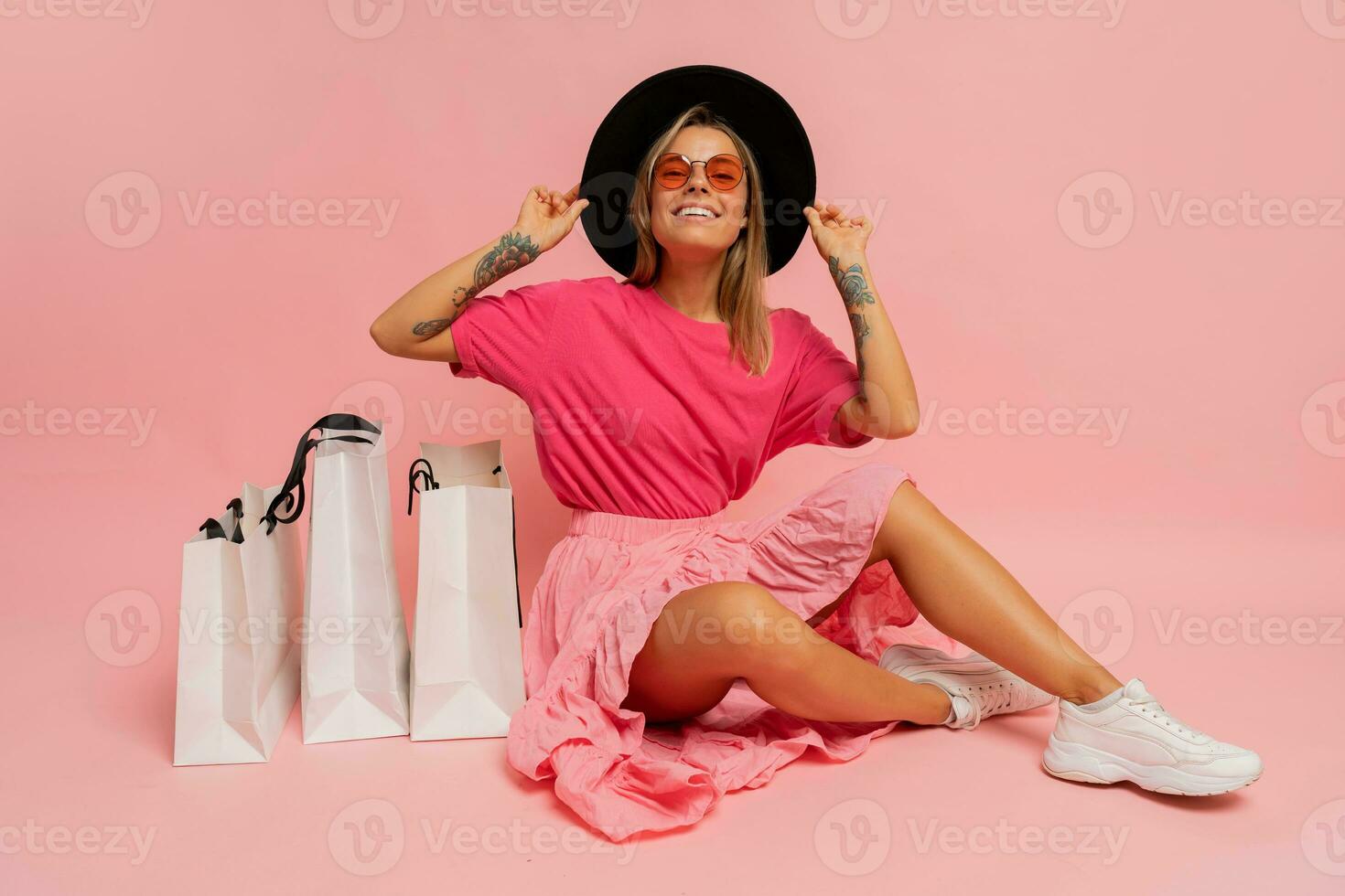 Pretty smiling woman in  spring trendy outfit posing with white shopping bags in studio over pink background. photo