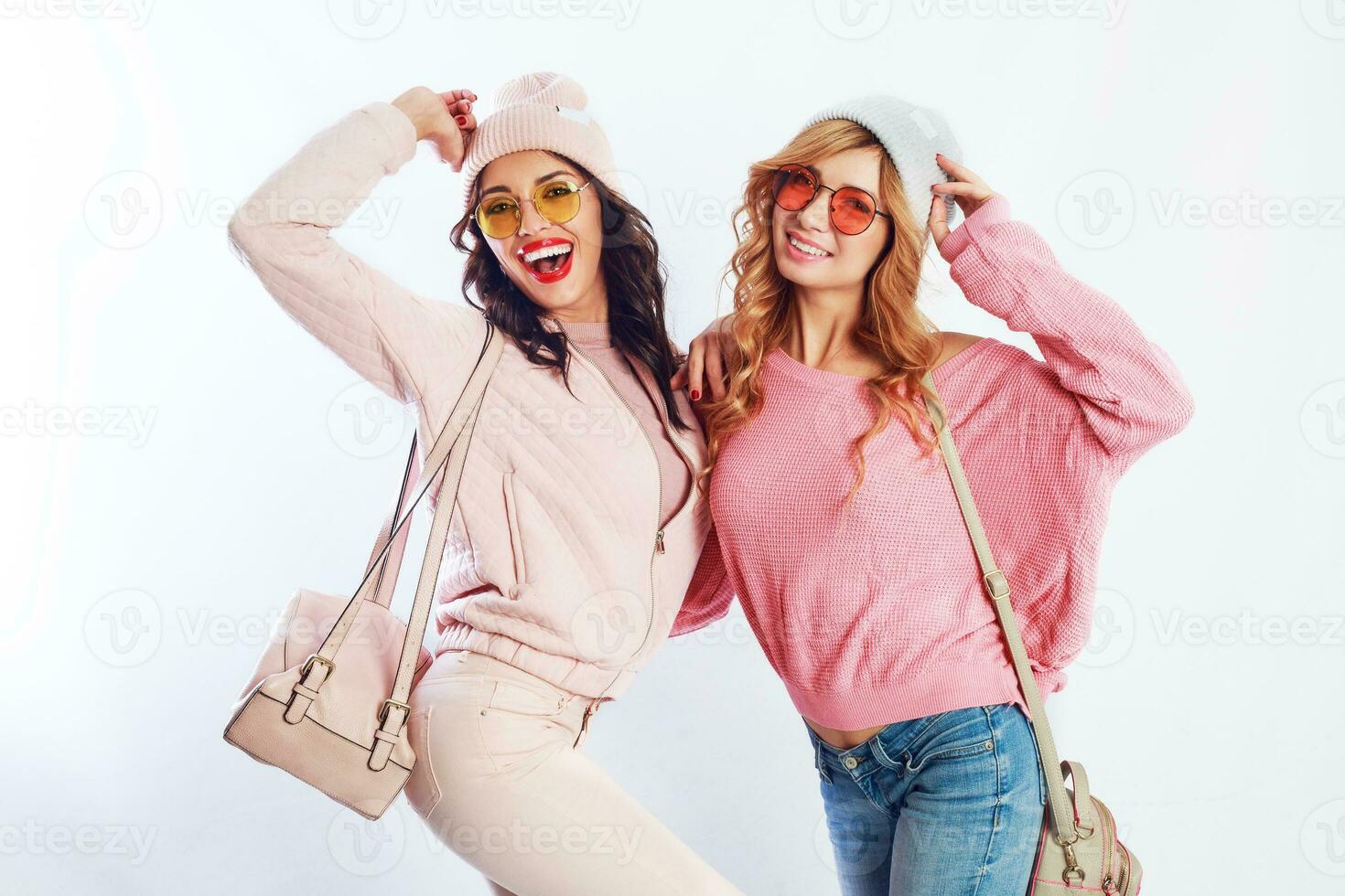 image of two girls, happy friends in stylish pink clothes and hat spelling funny  the together. White background. Trendy hat and glasses.Showing peace. photo