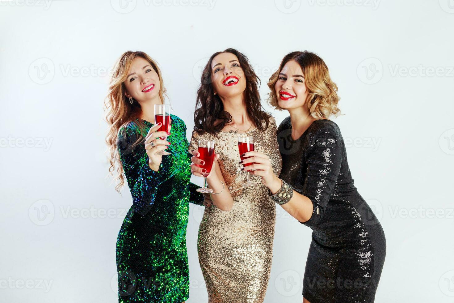 Three celebrating women in sparkly  evening outfit  enjoying  time together , drinking wine and dancing. White background. photo