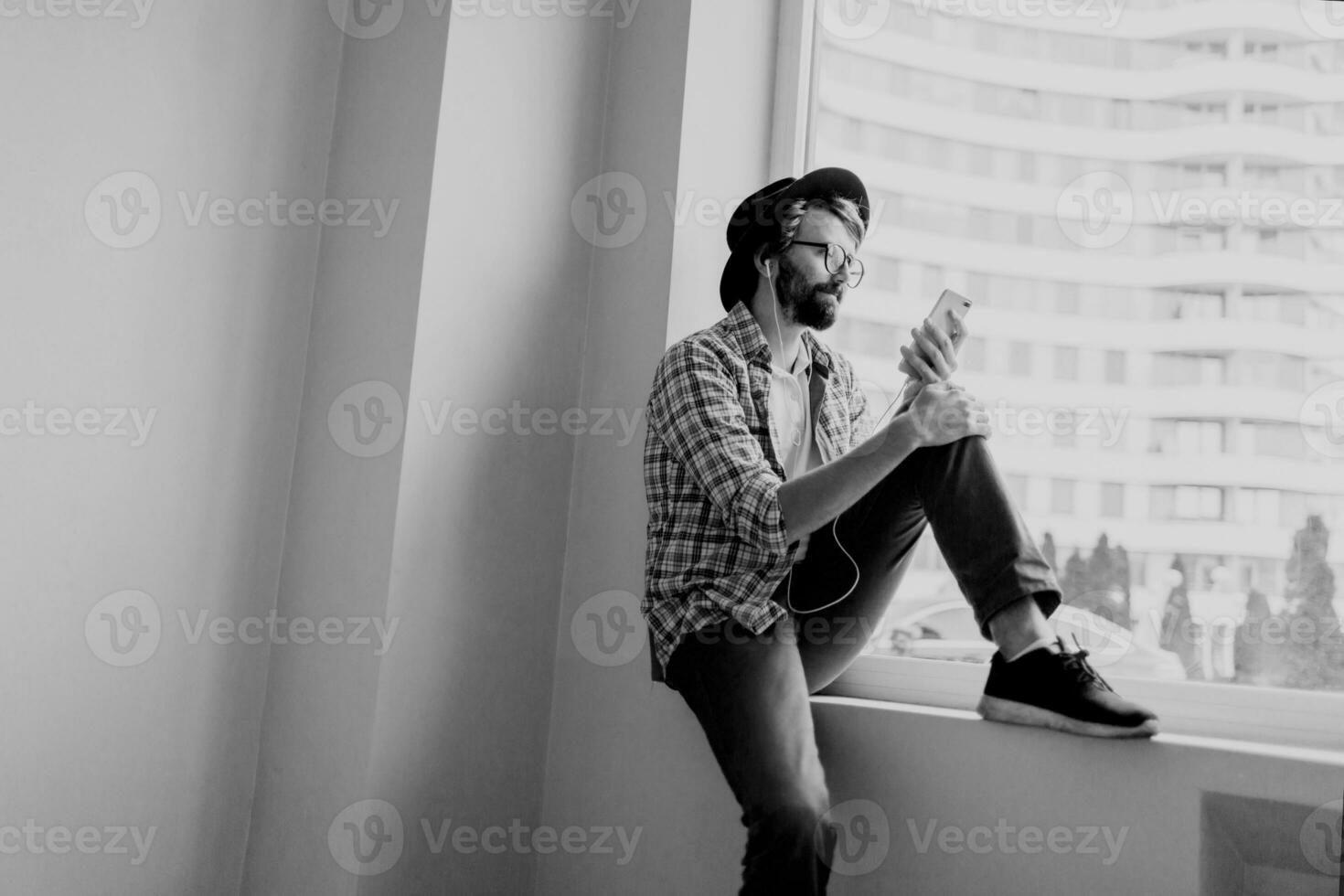 bearded man in bright checkered shirt installing new mobile application  on smartphone device and listening music. Hipster style. photo