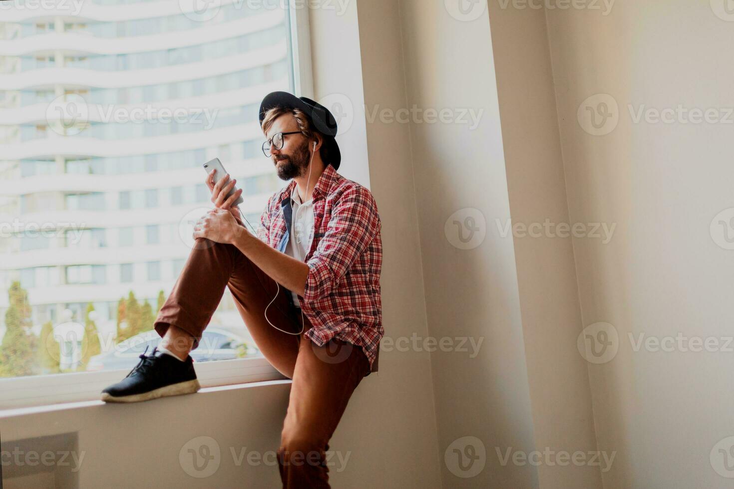 Stylish  bearded man in bright checkered shirt installing new mobile application  on smartphone device and listening music. Hipster style. photo