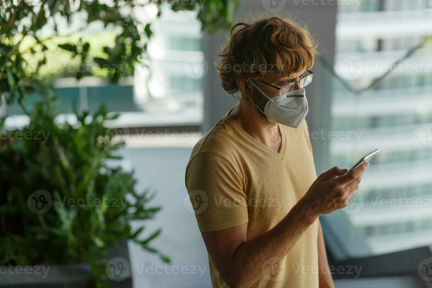 White bearded adult man using smartphone while wearing surgical mask on an industrial wall. Health, epidemics, social media. photo