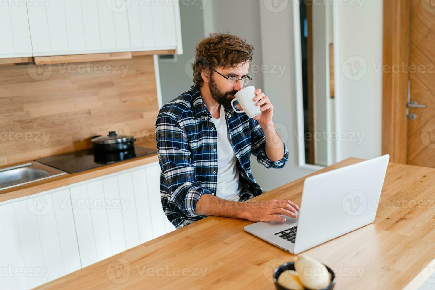 Handsome man freelancer using laptop studying online working from home, happy casual guy typing on  notebook surfing internet looking at screen enjoying distant job sit at table. Drink tea. photo